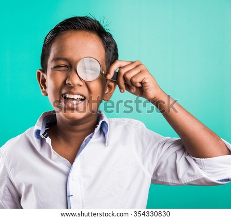happy indian school kid / boy with magnifying glass, standing isolated over green background