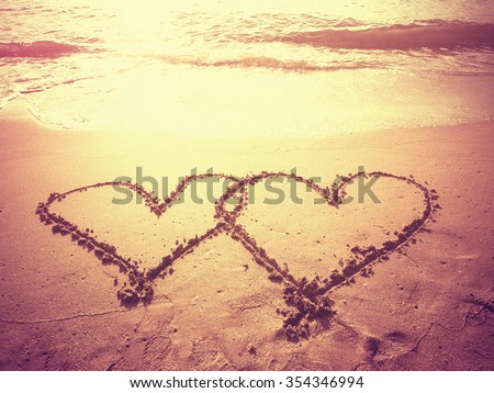 Vintage style photo of two hearts shape draw on the sand of a beach in morning time. Concept for love or wedding ceremony. Filtered process.