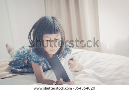 Vintage tone of Young Girl Lying On Her Bed and Reading A Book with nature light from window.