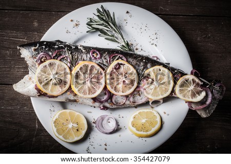 Fish Nelma with lemon, onion and rosemary on a wooden table. Toned.