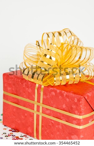 red gift box with gold ribbon and bow on white paper background.