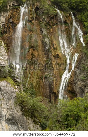 Photo of beautiful waterfalls cascades falling down from mountain wall rock surrounded by picturesque green rich foliage on natural landscape background, vertical picture