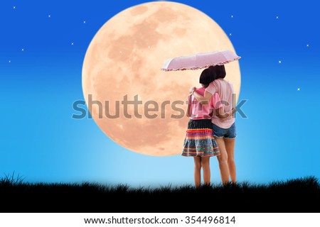 Mother and daughter standing reach an umbrella as the night full moon