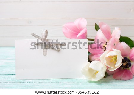 Postcard with fresh spring flowers and empty tag for your text on turquoise painted planks against white wall. Selective focus.