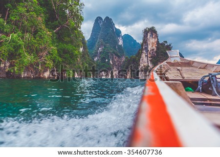 Small wooden tropical brown boat crossing the ocean and cutting waves against against background with moutntains, haze and tropical forest. Samui, Thailand. 
