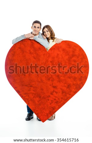 Romantic photo of beautiful couple on white background. Handsome young man and beautiful woman  standing behind big glitter heart