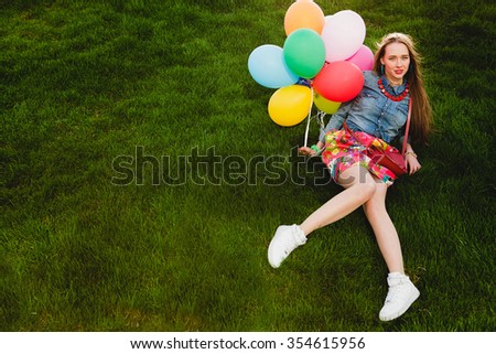 young stylish hipster teen girl happy, lying on grass in park, air balloons birthday party, cool accessories, colorful skirt, having fun, denim shirt, fashion trend summer outfit