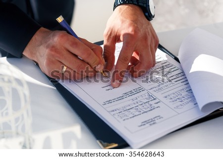 Happy groom signing wedding certificate on white table closeup, Santorini