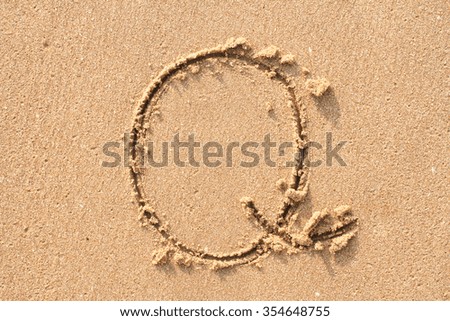 character Q handwritten on sand.