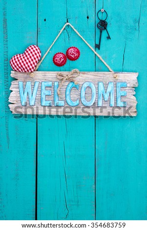 Rustic wood welcome sign with red fabric heart, black iron skeleton keys and cherry soda bottle caps hanging on antique teal blue wooden background