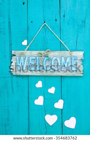 Wood welcome sign with pink cascading hearts hanging on rustic teal blue antique wooden background
