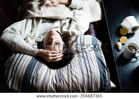 Sick woman in bed,calling in sick,day off from work.Thermometer to check temperature for fever.Vitamins and hot tea in front.Flu.Woman Caught Cold.Virus.Sick woman laying in bed under wool blanket  Royalty-Free Stock Photo #354687365