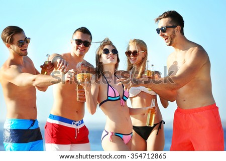 Happy young friends drinking beer at the beach, on sky background
