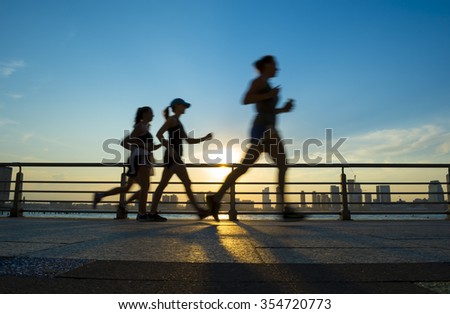 Motion blur silhouettes of joggers running at sunset on the Hudson River boardwalk in New York City