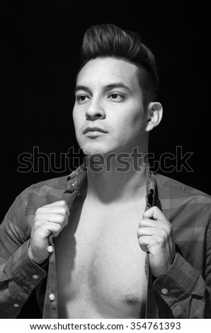 Hispanic male putting on square pattern shirt, arms covered open chest, black and white edition.