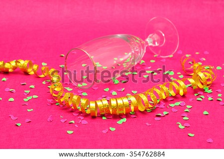Confetti and a gift ribbon displayed on a pink background with a champagne glass