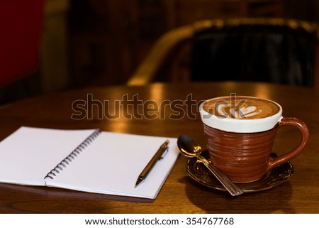 Hot latte art coffee cup on wooden table and note book.
