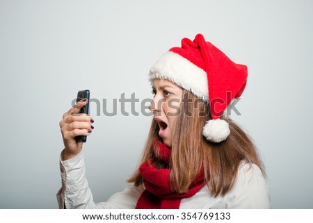 Santa girl looking shocked to phone. Christmas hat isolated portrait of a woman on a gray background.