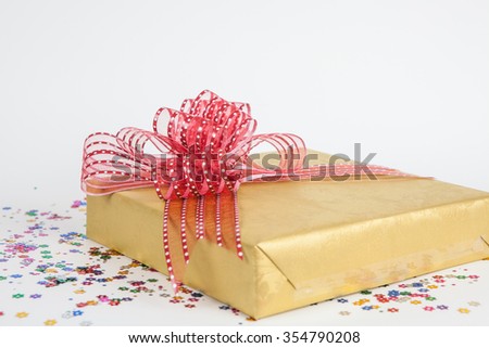 Beautiful gold present box with red bow on white paper backgound