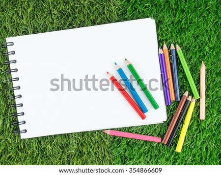 Blank white paper with color pencils on artificial grass.