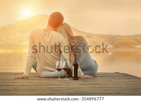 Romantic Couple sitting on the pier with red wine. Royalty-Free Stock Photo #354896777