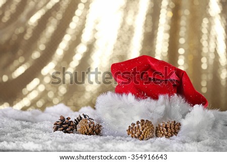 Santa Claus red hat with pine cones on the artificial snow against golden background, close up