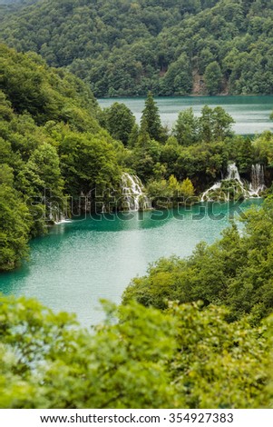 Photo of beautiful lakes with cascades waterfalls surrounded by picturesque verdurous mountains grown thickly forest with green trees on natural landscape background, vertical picture