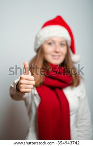 Santa girl showing thumbs up, everything is OK. Christmas hat isolated portrait of a woman on a gray background, studio photo.