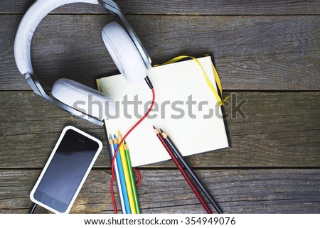 wooden desk table with smartphone, notepad (open note-book), headphones Colored Pencils. Top view with copy space. Concept for website banner, creation  background. Toned image