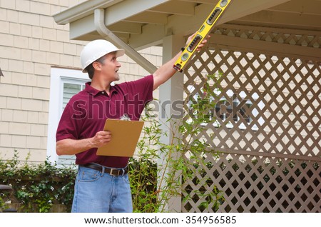 A home inspector or house building repair contractor in a hard hat holding a level and a clipboard outside a home doing an inspection or construction quote Royalty-Free Stock Photo #354956585