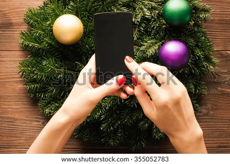 Female hands with red manicure holding a mobile phone with a touch screen on the background of Christmas decorations