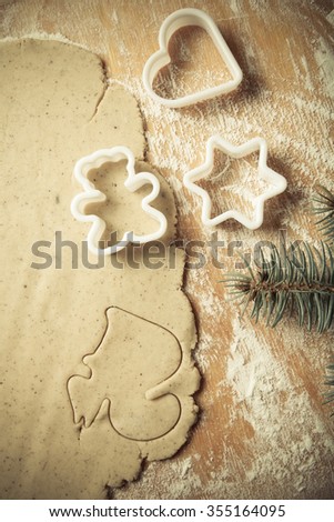 Dough for gingerbread cookie and cookie cutters in different shapes on light wooden cutting board like background. Toned.