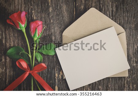Blank white greeting card with brown envelope and red rose flowers with ribbon bow on wooden table with vintage and vignette tone - Valentine and love concept Royalty-Free Stock Photo #355216463