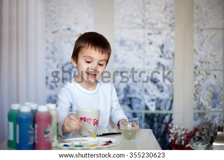 Cute little preschool boy, drawing picture on mug for his fathers birthday at home, wintertime