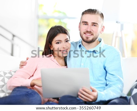 Happy couple sitting on sofa and working on a laptop