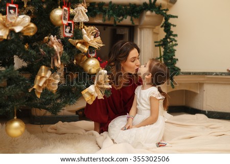 Cute young mom and kid kissing at home near the christmas tree in decorated room