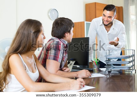 Salesman with young couple signing business contract in the office