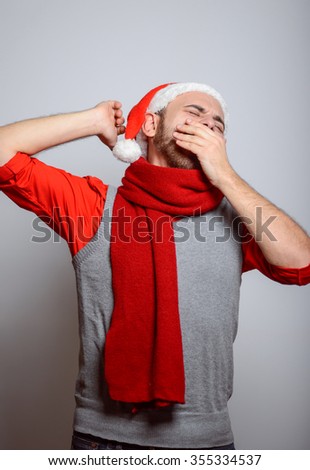 A man yawns. Happy Businessman wearing a Santa hat on New Year's corporate parties. Studio photo, isolated on a gray background