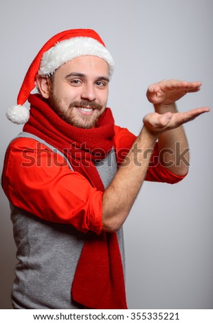 A man holding something invisible in her arms. Happy Businessman wearing a Santa hat on New Year's corporate parties. Studio photo, isolated on a gray background
