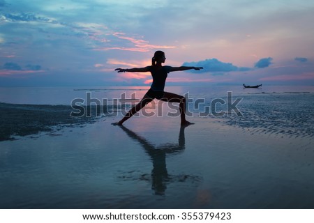 Silhouette of a young woman practicing yoga on the beach at sunrise Royalty-Free Stock Photo #355379423