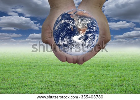 Planet in human hand over blurred beautiful blue sky and green grass background. Earth Day, Elements of this image furnished by NASA.