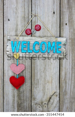 Rustic welcome sign with country red fabric hearts and red soda bottle caps hanging on antique wooden background