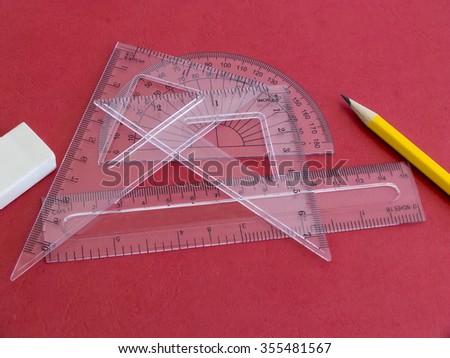 Protractor, rulers, pencil and eraser on red.