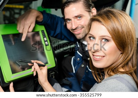 Auto mechanic is guiding an attractive female trainee in checking the car performance with a digital device. Concept for the fact that more and more women participate in jobs previously typical for