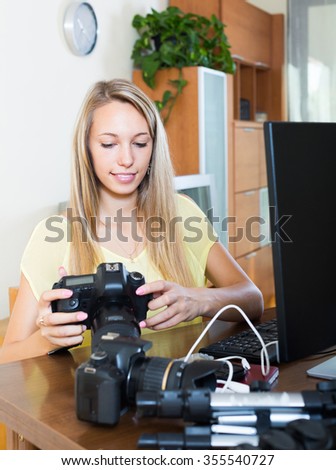Happy professional camerawoman sitting in front of laptop with camera
