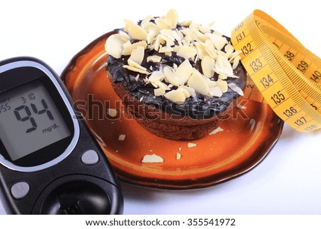 Glucose meter, homemade delicious fresh baked chocolate muffins with sliced almonds on brown plate and tape measure, concept for diabetes, slimming and dessert