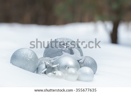 Silver grey shiny Christmas ornaments with Santa's ninth reindeer on snowy ground at winter forest background