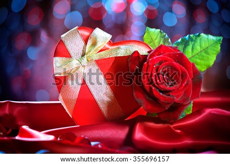 Valentine Red Heart Gift box and Red Rose Flower on Red Silk Background over glowing holiday background. St. Valentine's Day card design. Love