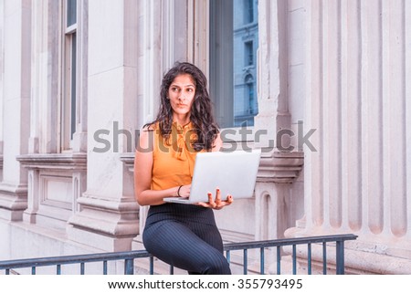 East Indian American Business Woman working in New York. Wearing sleeveless orange shirt, a college student sitting by office building, reading, working on laptop computer. Photo stylized effect.
