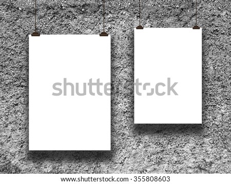Close-up of two hanged paper sheet frames with clips on rough concrete wall background